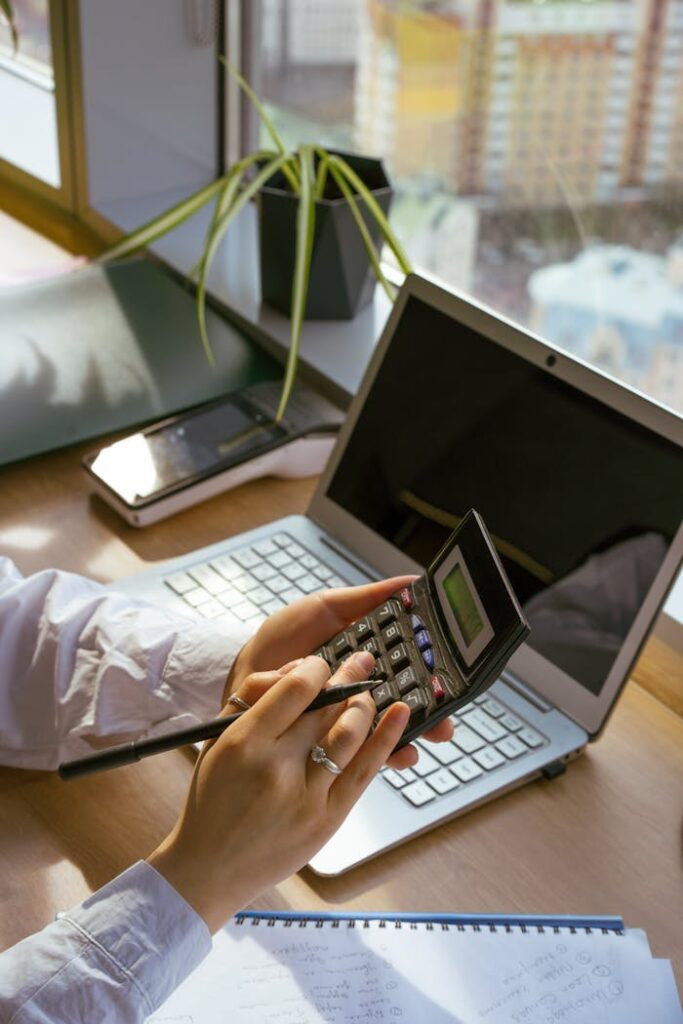 pexels-photo-8296991 Person calculating at desk with laptop and notebook. Ideal for business and finance themes.